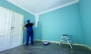 Man in a working overall is painting the wall in white color